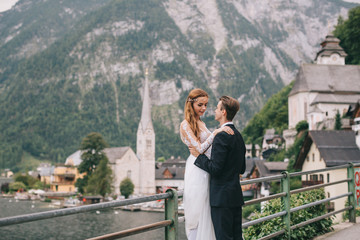 Fototapeta na wymiar A beautiful wedding couple walks on a background old cathedral, lake and mountains in a fairy Austrian town, Hallstatt.