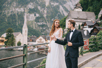 A beautiful wedding couple walks on a background old cathedral, lake and mountains in a fairy Austrian town, Hallstatt.