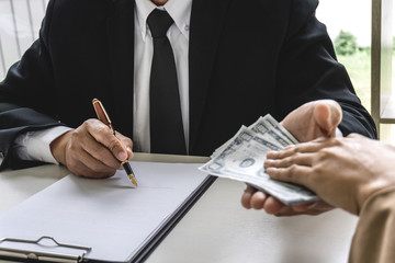 Business woman giving bribe money the form of dollar bills to mature counselor while give success...
