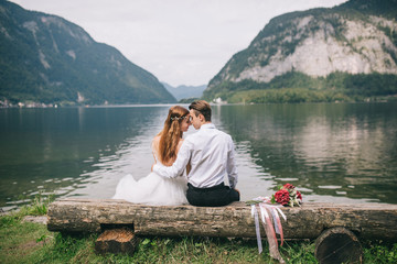 A wedding couple sits on the shore of a lake in the fairy-tale town of Austria, Hallstatt.