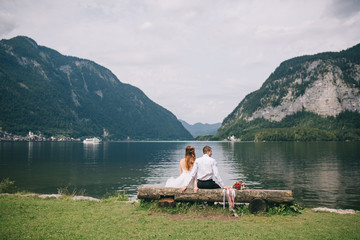 A wedding couple sits on the shore of a lake in the fairy-tale town of Austria, Hallstatt.