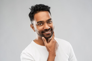 grooming and people concept - smiling indian man touching his beard over gray background