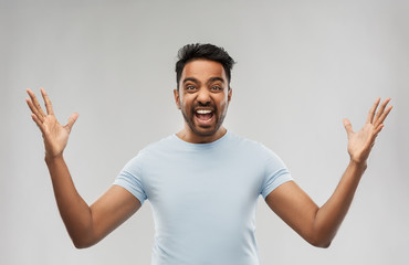 success, emotion and expression concept - happy young indian man celebrating victory over grey...