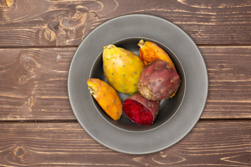 Lot of slices of fresh bright prickly pear opuntia on grey ceramic plate flatlay on brown wood