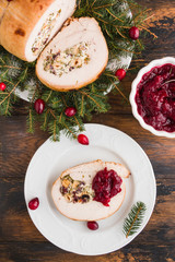 Stuffed  turkey breast roll with cranberry sauce on white plate on rustic wooden table, top view