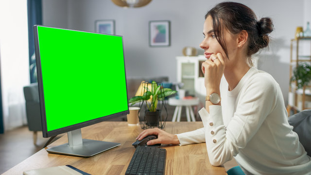 Beautiful Young Girl Works on a Green Mock-up Screen Personal Computer while Sitting at Her Desk in the Cozy Apartment.