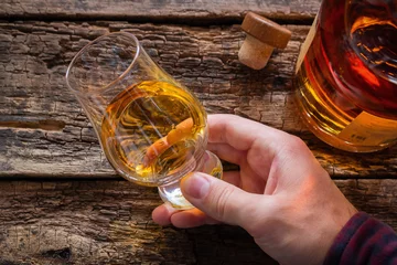 Fototapete hand holds whiskey in a glass for tasting on a wooden background © itakdalee