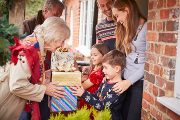 Grandparents Being Greeted By Family As They Arrive For Visit On Christmas Day With Gifts