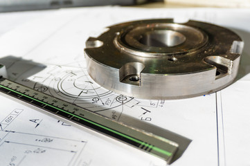 The transition flange after processing lies on the technical drawing. Next to the part is the measuring tool, a caliper.