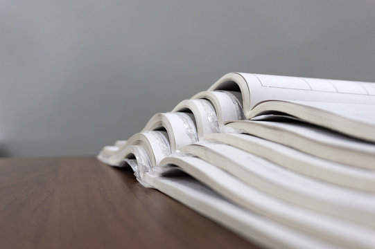 Open magazines lie on top of each other on a brown table, documents are stacked close-up.