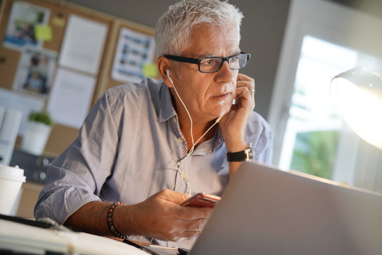 Mature man in office, using smartphone and earphones