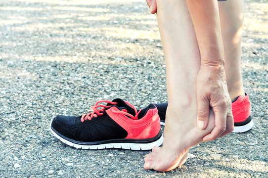 Pain In The Foot.Running Injury Leg Accident- Sport Woman Runner Hurting Massaging Painful Sprained Ankle In Pain.Athlete Woman Has Heel Injury, Sprained Ankle During Running Training.