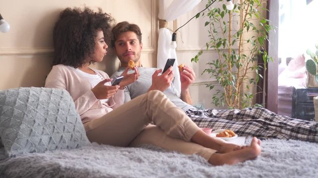 Couple using mobile phone while having breakfast in bed