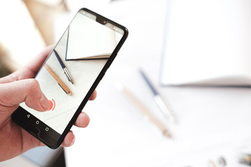 Mann hält Smartphone in der Hand und fotografiert/filmt den Arbeitsplatz. (Business - office)