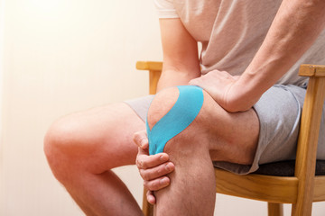 Man sitting on the chair and holding his sore knee with Kinesiology tape