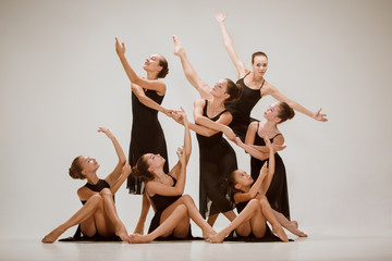 The group of modern ballet dancers dancing on gray studio background