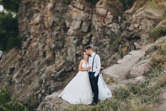 Beautiful newlyweds hugging against the backdrop of rocks and mountains. Stylish bride and beautiful bride are standing on the cliff. Wedding portrait. Family photo.