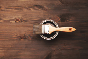Paintbrush and a newly opened can of grey paint on fresh painted wooden surface