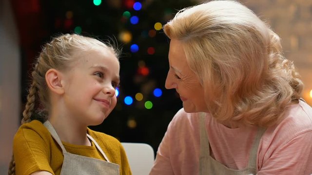 Granny kissing granddaughter on cheek, visit of relatives on Christmas holidays