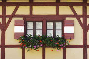 Part of house wall with window in traditional German fachwerk (timber framing) style  with red and white shutters and flowers in Nuremberg