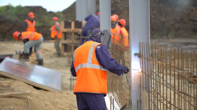 Industrial worker welding of metal structures, welder man male worker soldering steel beam structure on new building on construction site. welder working. Sparks fly as one welder welds steel. 4 K