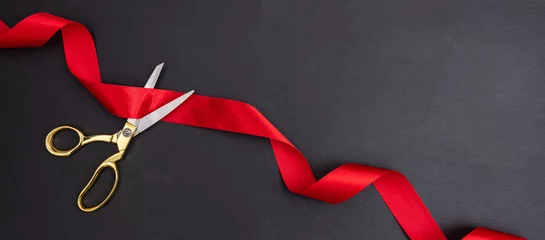 Fotobehang Scissors cutting red silk ribbon against black background, banner. © Rawf8