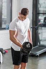 Fototapeta na wymiar handsome muscular bodybuilder exercising with dumbbell in gym