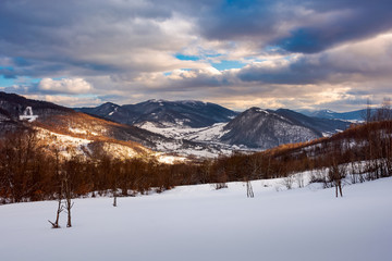 Fototapeta na wymiar beautiful winter landscape of Carpathians. Village down in the valley in dappled light. gorgeous evening cloudy sky above the ridge.