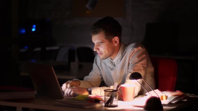 Pretty caucasian guy is typing on laptop , looking at screen precisely with great yawn, lante time in dark office, shadows, workaholic person illustration
