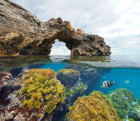 Rock formation natural arch with algae and fish underwater, split view half above and below water surface, Mediterranean sea, Cabo de Palos, Cartagena, Murcia, Spain