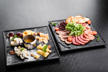 cold smoked meat plate with pork chops, prosciutto, salami and bread sticks on a black plate on a dark background