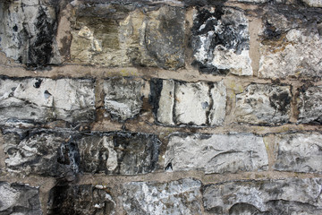 Close up of old gray irregular bricks wall with black stains. Natural dirty stones wall texture