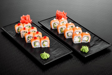 Philadelphia roll with salmon and cucumber. Maki Sushi set on dark pattern background. Sushi Set nigiri, rolls and sashimi served in black square plate. On dark pattern background.