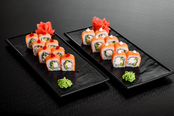 Philadelphia roll with salmon and cucumber. Maki Sushi set on dark pattern background. Sushi Set nigiri, rolls and sashimi served in black square plate. On dark pattern background.