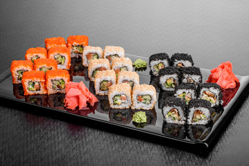 Maki Sushi set on dark pattern background. Sushi Set nigiri, rolls and sashimi served in black square plate. On dark pattern background.