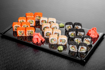 Maki Sushi set on dark pattern background. Sushi Set nigiri, rolls and sashimi served in black square plate. On dark pattern background.