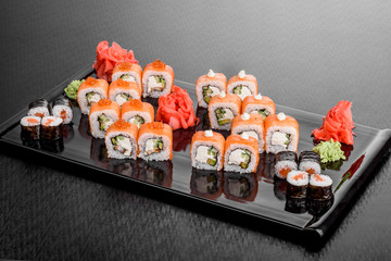 Maki Sushi set on dark pattern background. Sushi Set nigiri, rolls and sashimi served in black square plate. On dark pattern background.