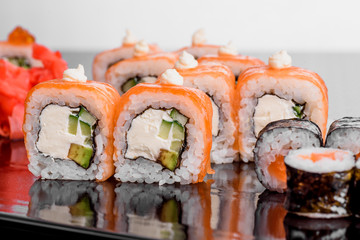 Philadelphia roll with salmon and cucumber. Maki Sushi set on dark pattern background. Sushi Set nigiri, rolls and sashimi served in black square plate. On dark pattern background.