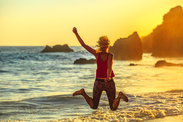 Joyful woman jumping on seashore of El Matador Beach near Malibu, California, United States. Female jumper between limestone formations on Pacific Ocean. Sunset light. California West Coast travel.
