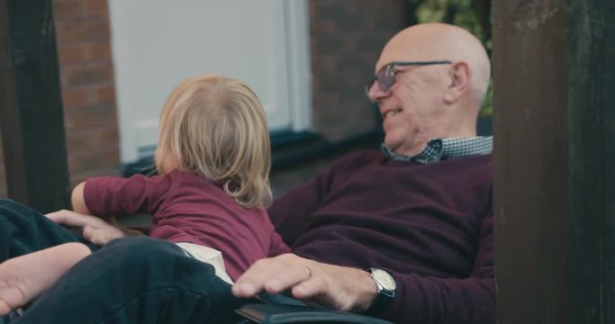 Little toddler sitting with grandfather on sunlounger