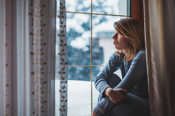 Sad woman sitting by the window looking outside
