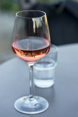 Shiny clean wine glass with pink-coloured rose wine reflecting spears of a surrounding fence...