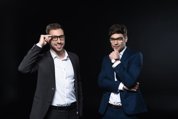 handsome young businessmen in stylish suits looking at camera isolated on black