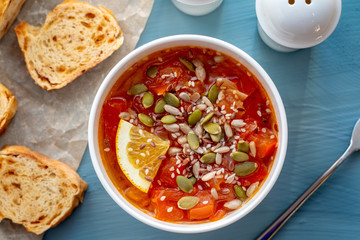 Tomato soup with lemon, seeds and bread on a blue background.