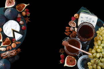 Frame of various wine snacks: Cheese plate with blue cheese, brie, truffle hard cheese with grapes, figs, honey, fruits and nuts isolated on black background. Top view