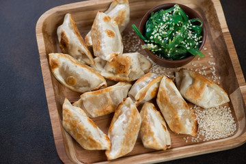 Closeup of a wooden serving tray with gyoza dumplings and seaweed salad, horizontal shot