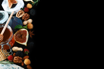Frame of various wine snacks: blue cheese, brie, grapes, figs, honey, fruits and nuts isolated on black background. Top view