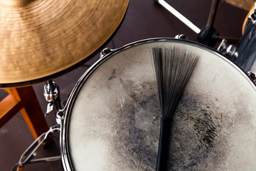 Fototapeta na wymiar Close-up of of black drum brush on a white shabby drum and а part of golden cymbal. Concept concert, live music, performance, musical evening in restaurant