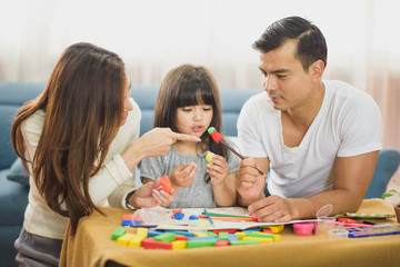Fototapeta premium Family time Daughter laughing enjoying playing with her father and mother on the table in front of sofa at home.