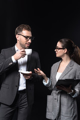 business people with cup of coffee and clipboard having conversation isolated on black